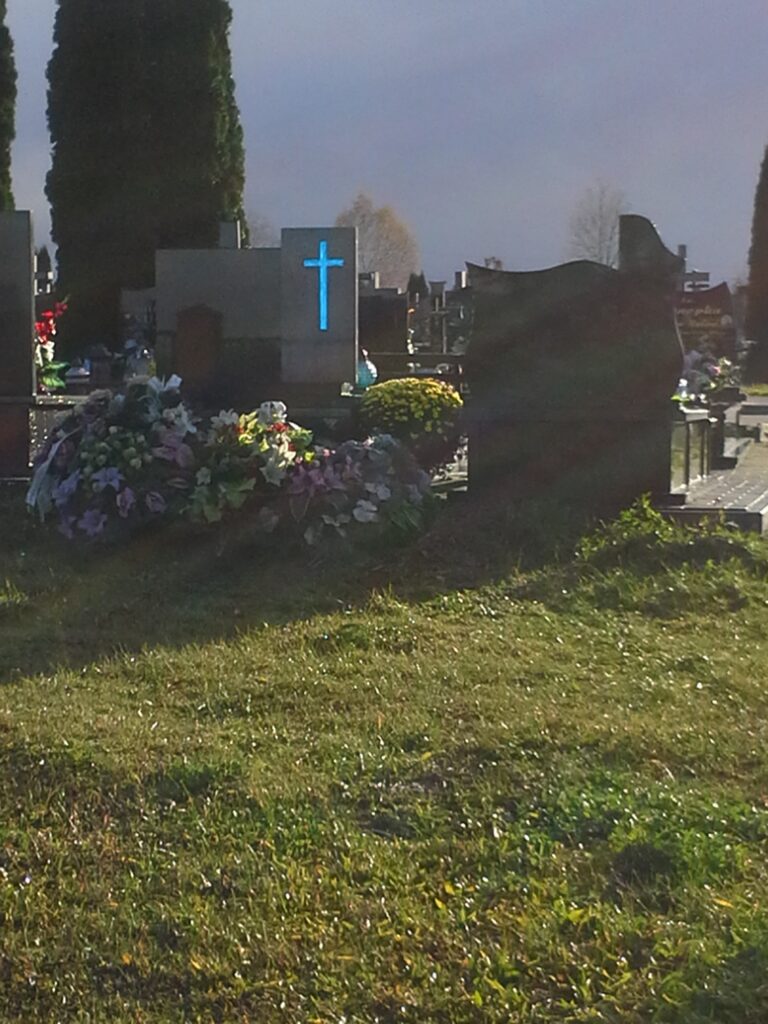 Szklany niebieski krzyż na pomniku podświetlony przez zachodzące słońce